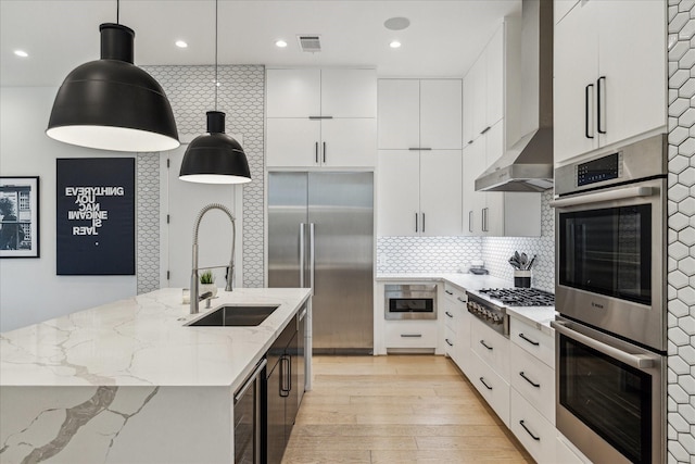 kitchen with wine cooler, appliances with stainless steel finishes, white cabinetry, wall chimney exhaust hood, and a sink