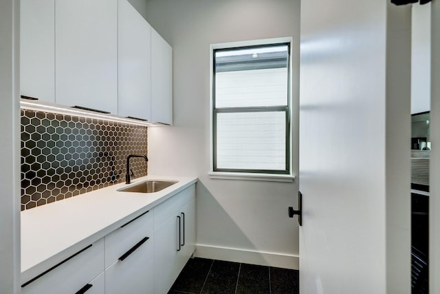 interior space featuring a sink, white cabinetry, light countertops, decorative backsplash, and baseboards