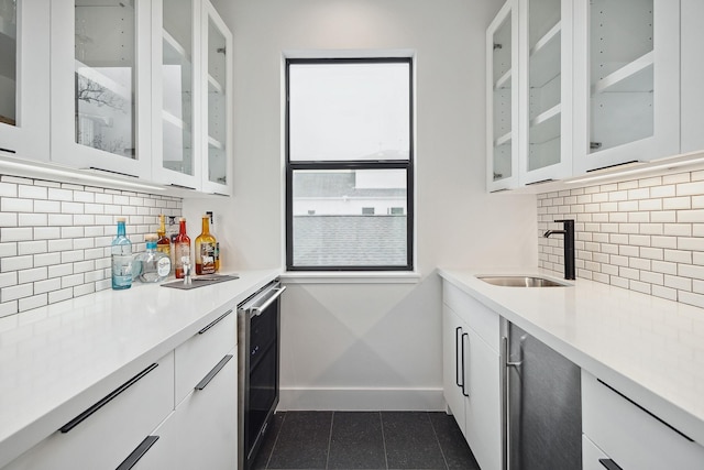 kitchen featuring tasteful backsplash, baseboards, light countertops, white cabinetry, and a sink