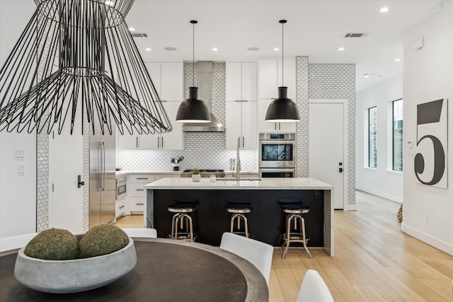 kitchen with visible vents, a kitchen island with sink, appliances with stainless steel finishes, light wood-type flooring, and backsplash