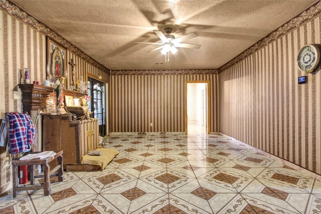 interior space featuring wallpapered walls, a ceiling fan, and a textured ceiling