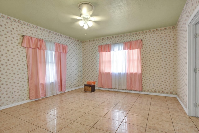 empty room with wallpapered walls, light tile patterned flooring, baseboards, and ceiling fan