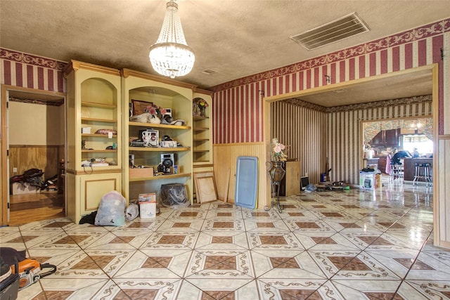 interior space featuring wallpapered walls, a textured ceiling, and wainscoting