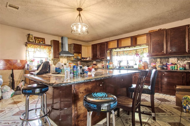 kitchen featuring visible vents, a breakfast bar area, decorative backsplash, an inviting chandelier, and wall chimney exhaust hood