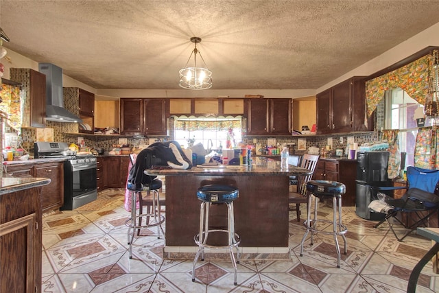 kitchen featuring stainless steel range with gas cooktop, dark countertops, wall chimney range hood, backsplash, and a center island