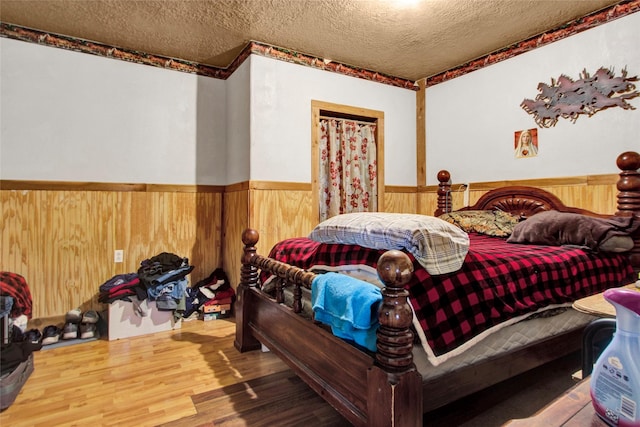 bedroom with wainscoting, a textured ceiling, wood walls, and wood finished floors