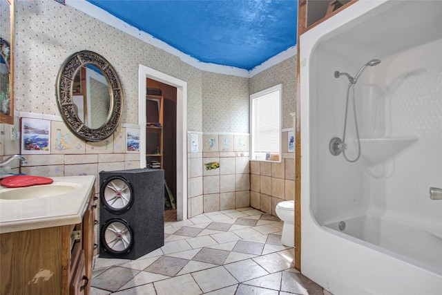 full bathroom featuring wallpapered walls, tile walls, toilet, wainscoting, and vanity