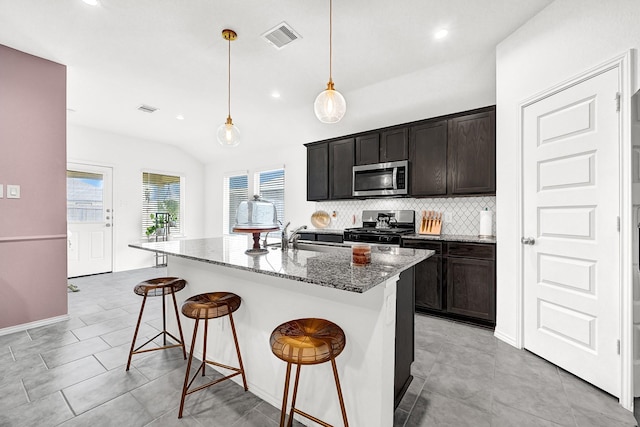 kitchen featuring visible vents, backsplash, light stone counters, appliances with stainless steel finishes, and a kitchen breakfast bar