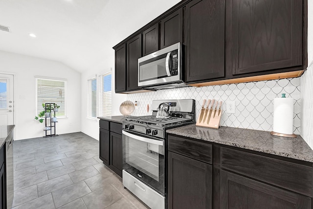 kitchen with stainless steel appliances, dark stone counters, light tile patterned floors, decorative backsplash, and lofted ceiling