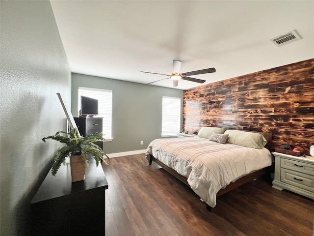 bedroom featuring visible vents, a ceiling fan, dark wood-style flooring, baseboards, and an accent wall