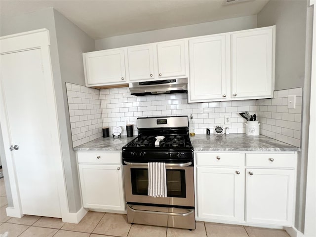 kitchen featuring stainless steel gas range oven, under cabinet range hood, white cabinets, light tile patterned floors, and decorative backsplash