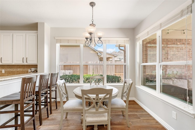 dining room featuring an inviting chandelier, a healthy amount of sunlight, light wood-type flooring, and baseboards