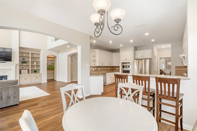 dining room with arched walkways, light wood finished floors, a tiled fireplace, and an inviting chandelier