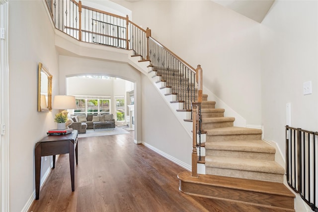 staircase featuring arched walkways, baseboards, a towering ceiling, and wood finished floors