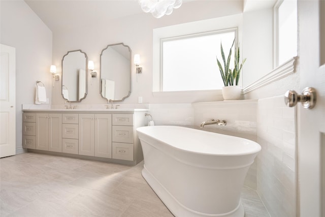 full bath featuring tile patterned floors, a sink, a freestanding bath, and double vanity