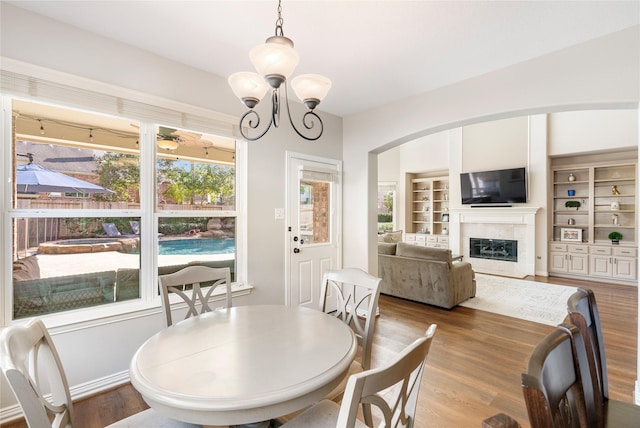 dining space with built in features, wood finished floors, arched walkways, a fireplace, and a chandelier