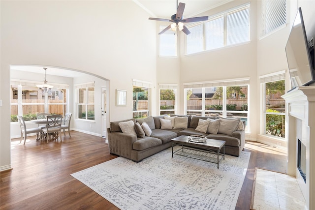 living area with baseboards, a fireplace with flush hearth, ceiling fan with notable chandelier, wood finished floors, and arched walkways