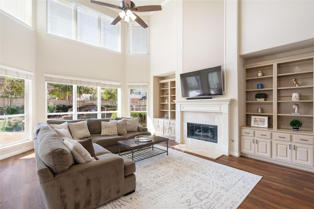 living room with a tiled fireplace, a healthy amount of sunlight, dark wood-type flooring, and a ceiling fan