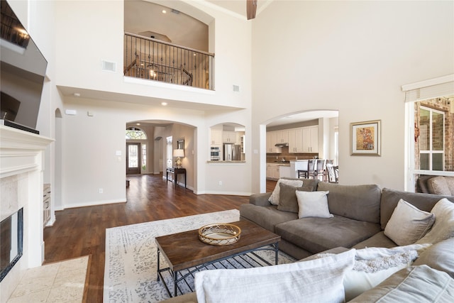 living area with visible vents, baseboards, dark wood finished floors, a fireplace, and arched walkways