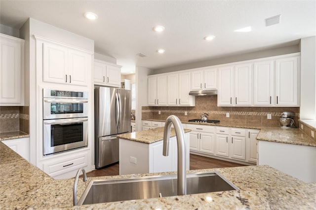 kitchen with light stone counters, a sink, stainless steel appliances, white cabinets, and under cabinet range hood