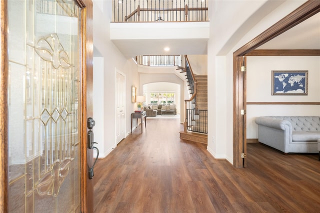 entryway featuring stairs, wood finished floors, arched walkways, and a towering ceiling