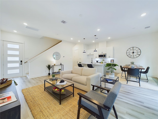 living room featuring stairs, light wood-style flooring, recessed lighting, and visible vents