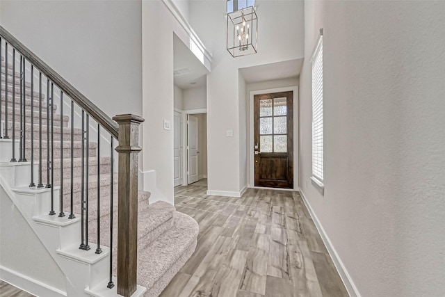 entrance foyer with wood finished floors, a towering ceiling, baseboards, a chandelier, and stairs