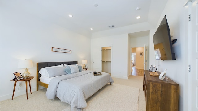 bedroom with a spacious closet, recessed lighting, light colored carpet, and baseboards