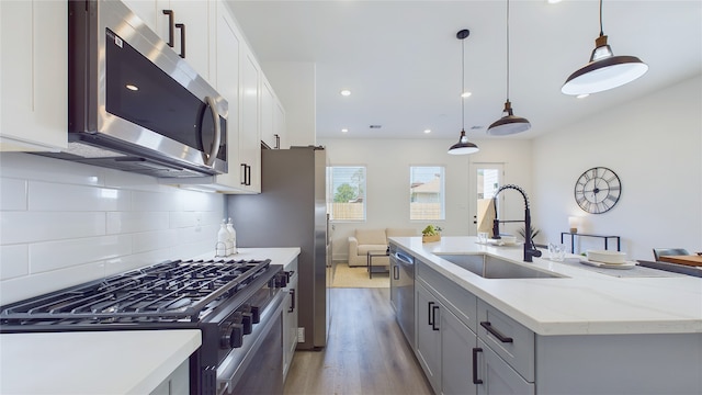 kitchen featuring a center island with sink, a sink, appliances with stainless steel finishes, light wood-type flooring, and backsplash