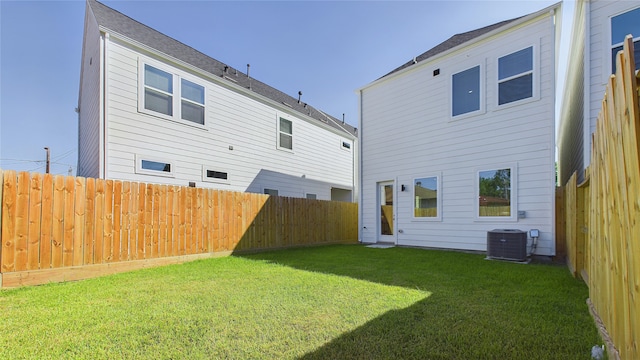 rear view of property featuring a lawn, central AC unit, and a fenced backyard