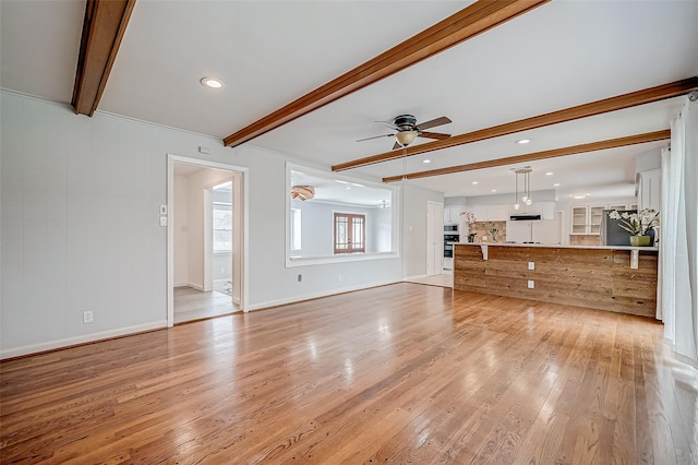 unfurnished living room featuring a ceiling fan, beam ceiling, light wood-style floors, and baseboards