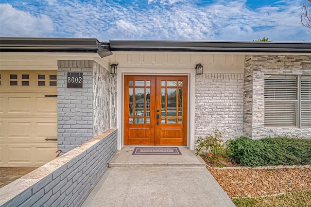 entrance to property featuring french doors, brick siding, and an attached garage