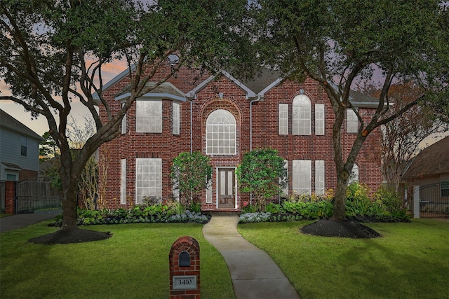 view of front of property with brick siding, a yard, and fence