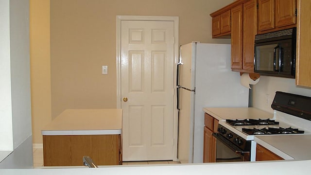 kitchen with light countertops, brown cabinetry, white gas range oven, and black microwave