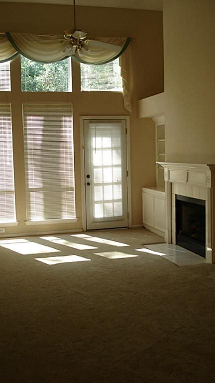 unfurnished living room with a tiled fireplace, carpet, and a towering ceiling