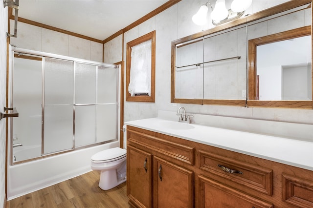 bathroom featuring vanity, wood finished floors, ornamental molding, toilet, and combined bath / shower with glass door