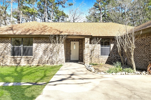 view of front of house with a lawn, brick siding, and a shingled roof