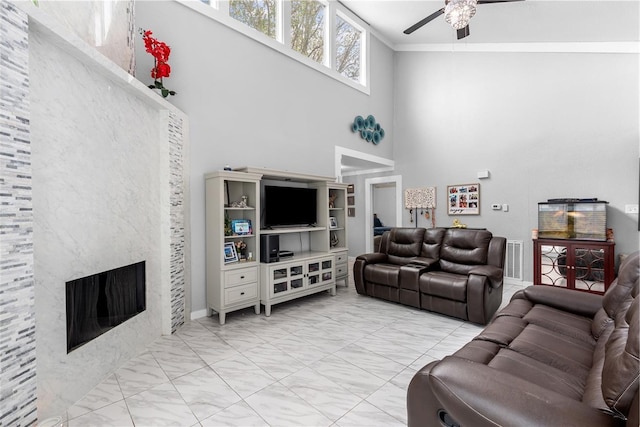 living area featuring visible vents, ceiling fan, ornamental molding, a towering ceiling, and a large fireplace