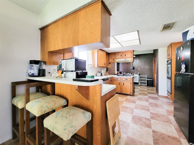 kitchen featuring visible vents, under cabinet range hood, a peninsula, appliances with stainless steel finishes, and light countertops