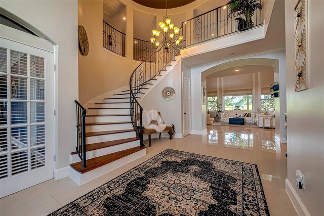 tiled foyer featuring baseboards, a high ceiling, arched walkways, stairs, and a notable chandelier