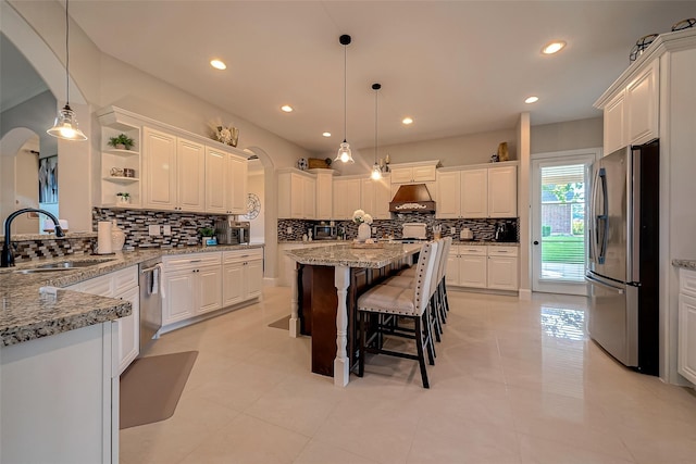 kitchen featuring a sink, a kitchen bar, appliances with stainless steel finishes, arched walkways, and open shelves