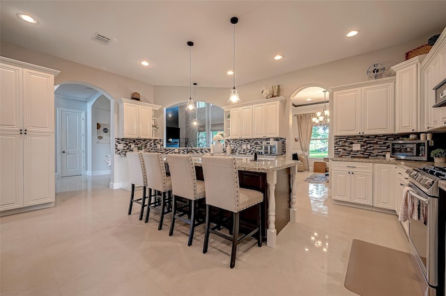 kitchen with arched walkways, stainless steel appliances, a kitchen bar, and light stone countertops