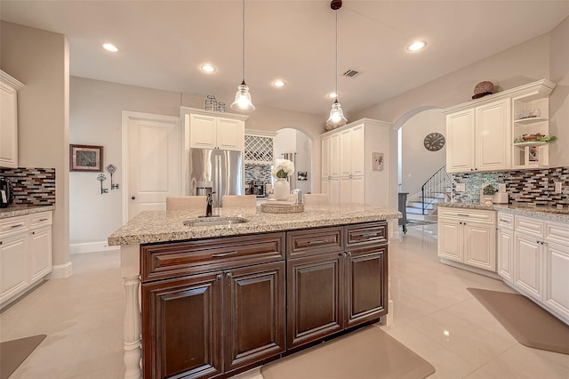 kitchen featuring visible vents, stainless steel fridge with ice dispenser, arched walkways, a sink, and white cabinetry