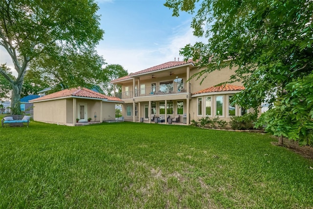 back of property with stucco siding, a lawn, a ceiling fan, a tile roof, and a balcony