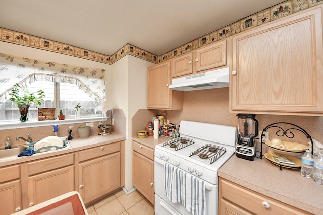 kitchen featuring light brown cabinets, under cabinet range hood, light countertops, light tile patterned floors, and white range with gas stovetop