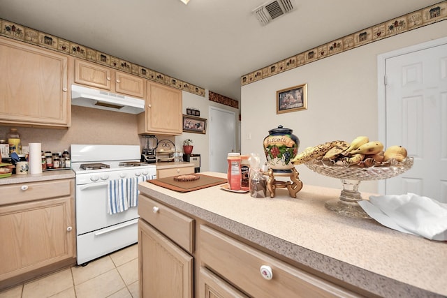 kitchen with light brown cabinets, under cabinet range hood, light countertops, white range with gas stovetop, and light tile patterned flooring