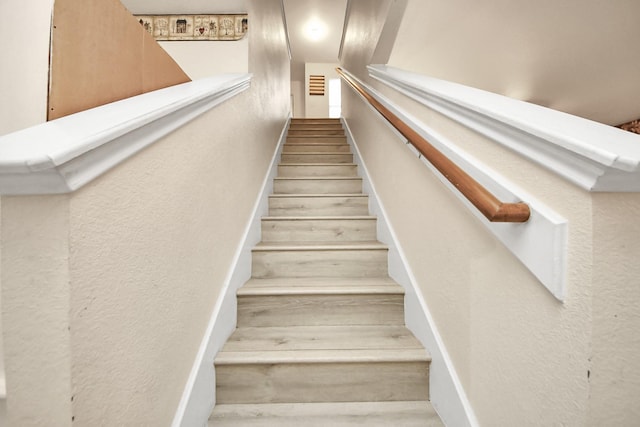 staircase with wood finished floors and a textured wall