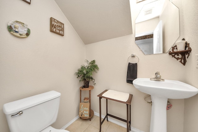 bathroom featuring baseboards, toilet, lofted ceiling, tile patterned floors, and a sink