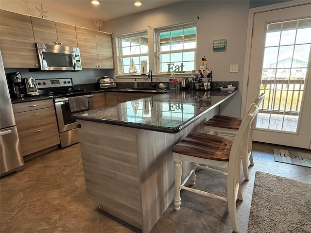 kitchen featuring dark stone counters, a breakfast bar area, appliances with stainless steel finishes, a peninsula, and a sink