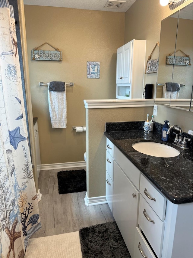 bathroom featuring visible vents, toilet, wood finished floors, baseboards, and vanity